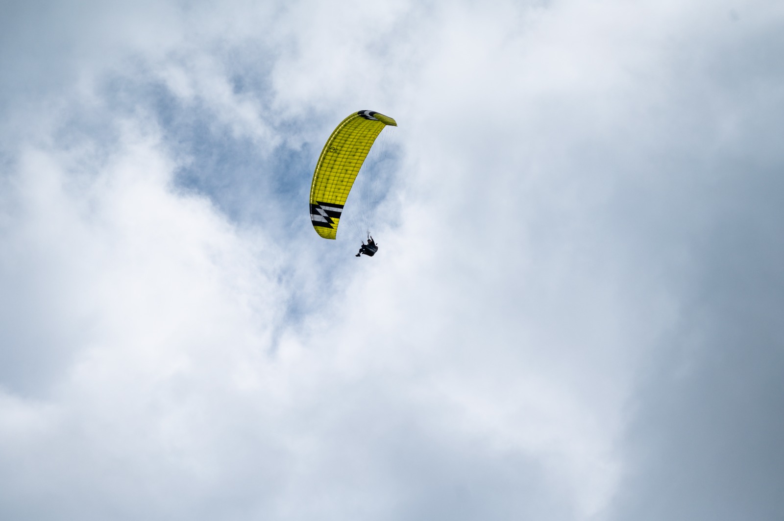 A paraglider with a yellow wing flying between the clouds